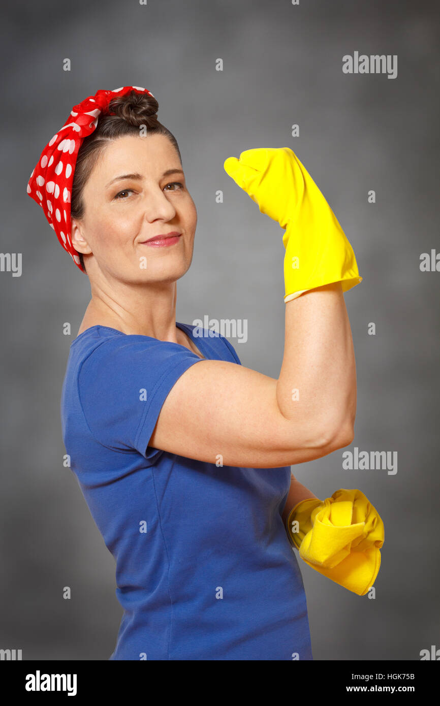 Felice donna delle pulizie con velo di colore giallo guanti per la pulizia e il panno, che mostra i suoi muscoli, indicando potente servizio di pulizia Foto Stock
