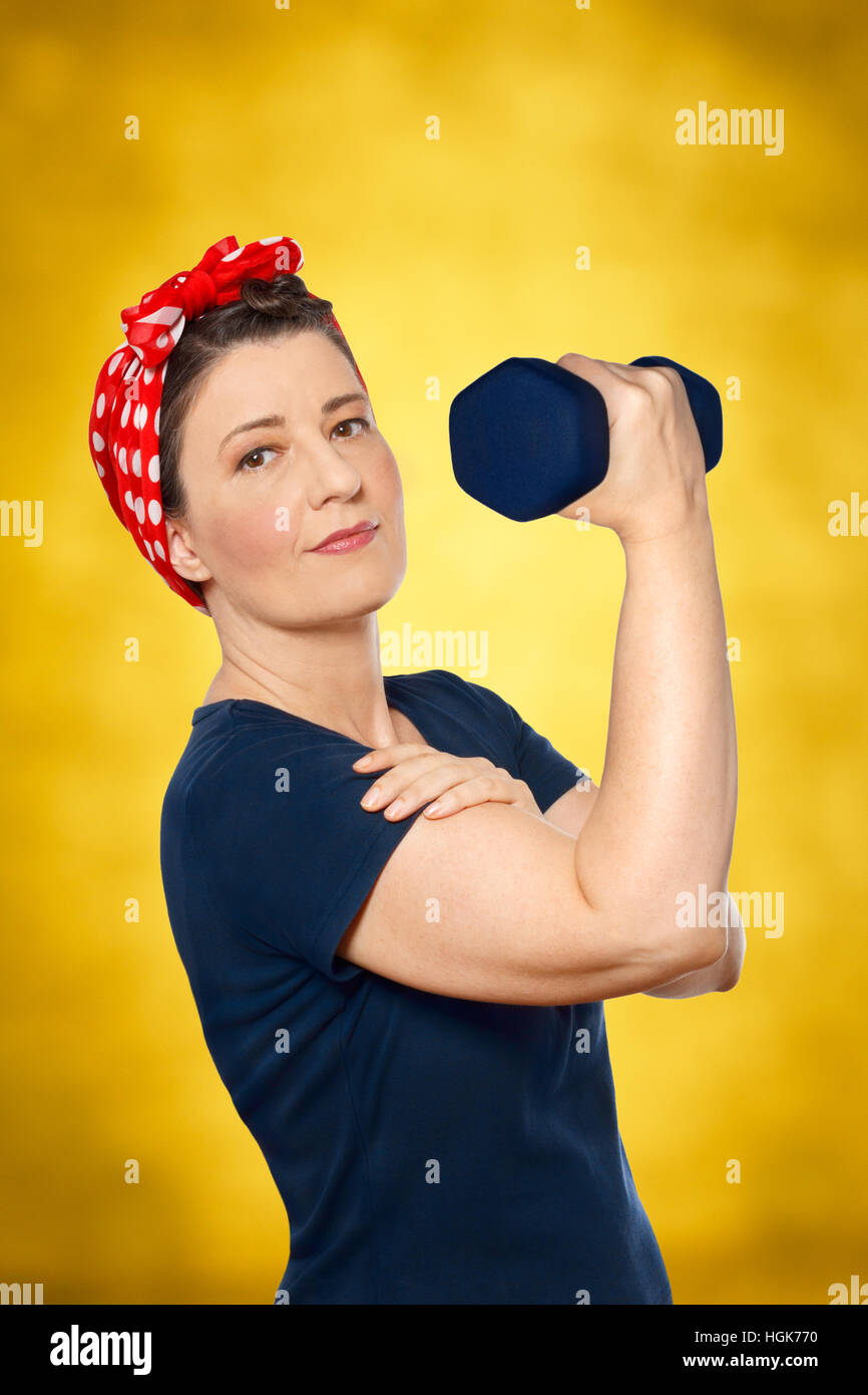 Donna sorridente con il fazzoletto rosso e blu t-shirt di sollevare un peso di fronte a sfondo giallo, icona americana Rosie la rivettatrice Foto Stock