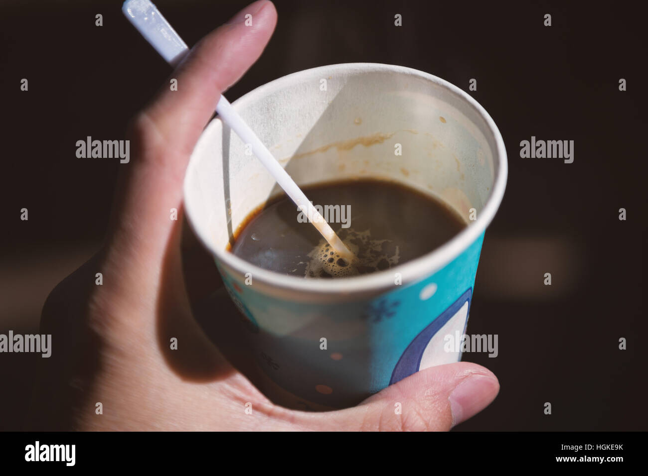 Messa a fuoco ravvicinata sul caffè nero all'interno del bicchiere di carta azienda dalla mano sinistra con sfondo scuro Foto Stock