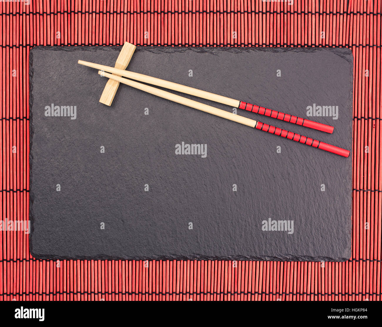 Bacchette sul nero ardesia coaster su red bamboo tovagliolo di scorrimento Foto Stock