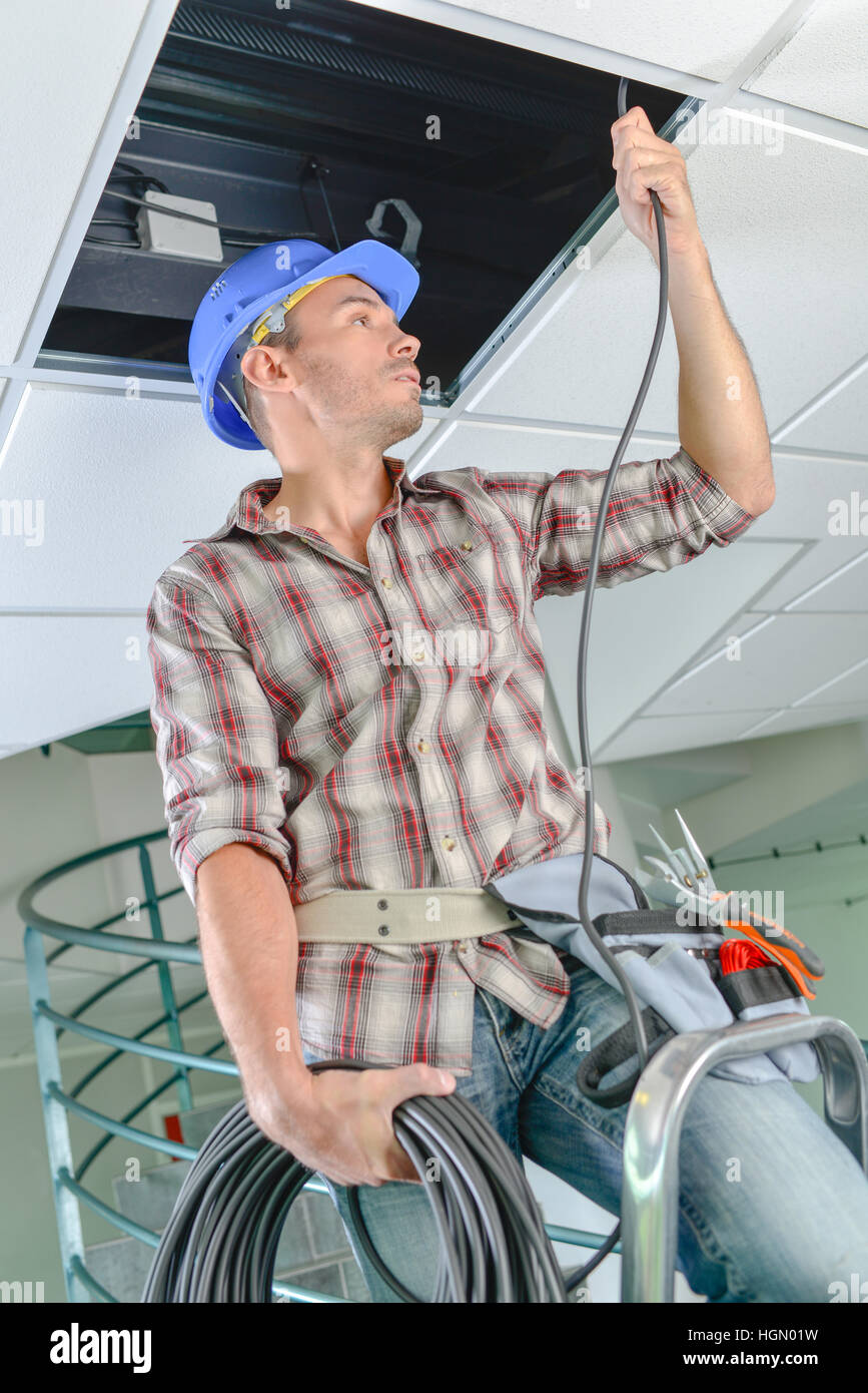 L'uomo l'inserimento del cavo nello spazio sopra il controsoffitto Foto Stock