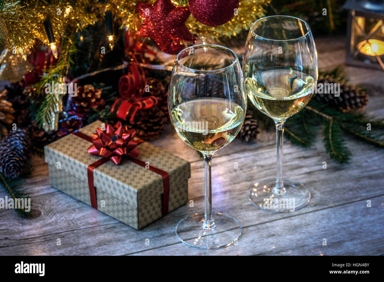 Due wineglas con vino bianco su una tavola di legno in background di albero di Natale, dono e candele Foto Stock