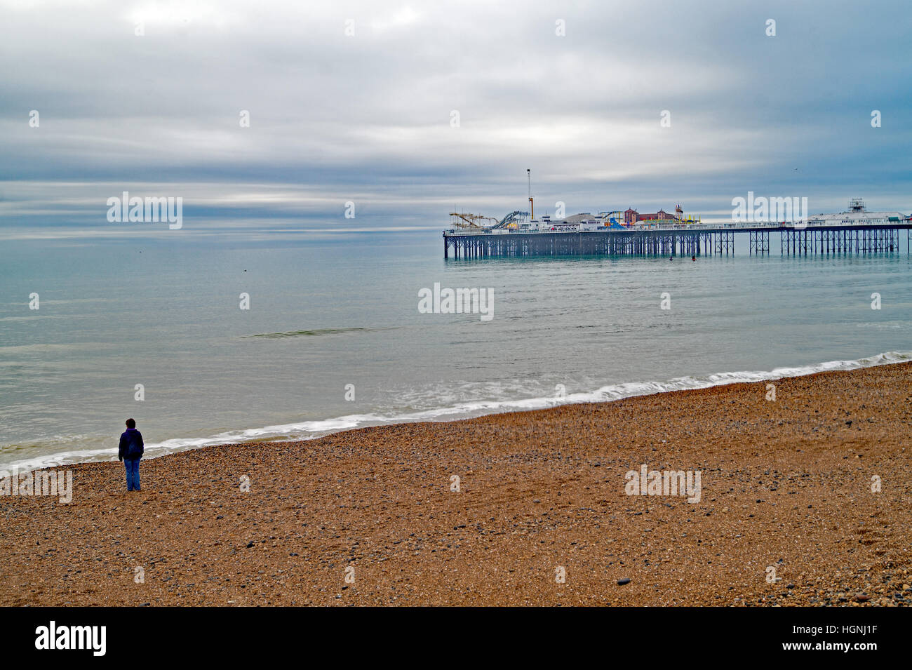 Una solitaria figura sulla spiaggia guardando al Molo di Brighton su una giornata invernale e Foto Stock