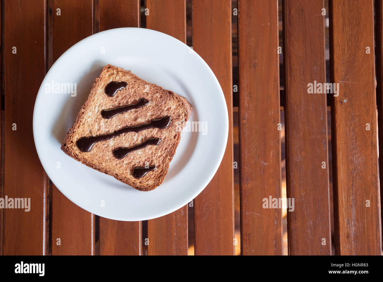 Cioccolato da spalmare sul pane tostato nel disco bianco sul tavolo in legno luce della finestra Foto Stock