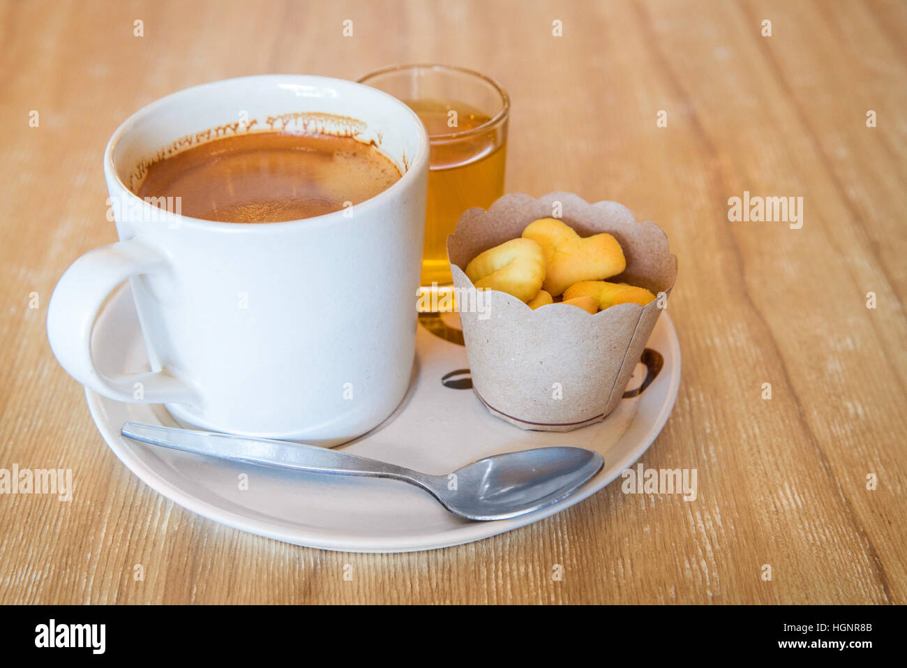 Caffè in tazza bianca sul disco con piccole cookie sul tavolo di legno, finestra spia Foto Stock