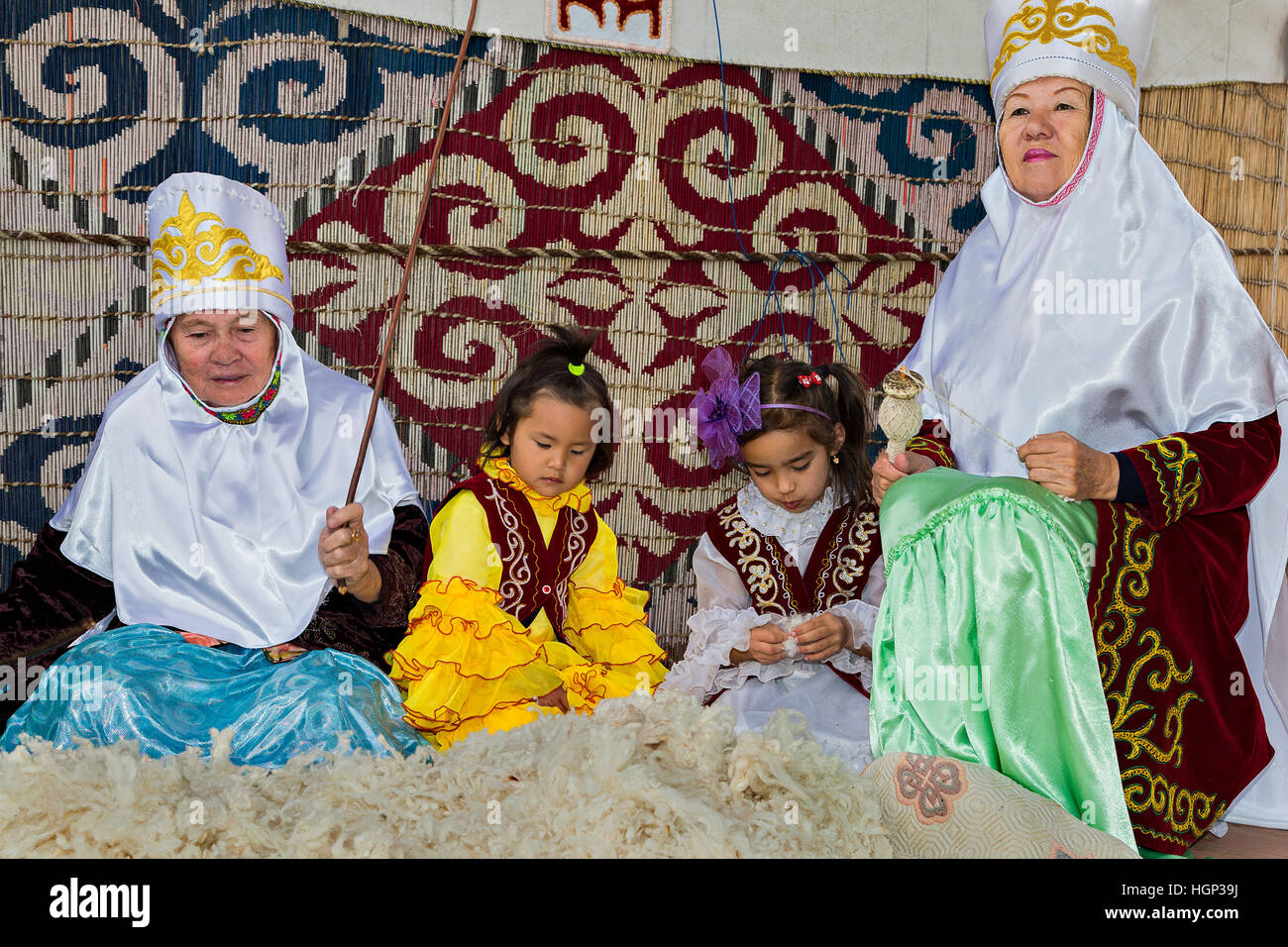 Le donne e i bambini kazaki si siedono insieme e una donna tocca la lana per renderla soffice. Foto Stock