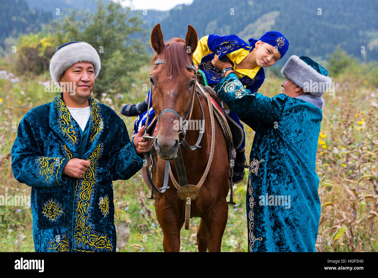 Il kazako uomo in costumi nazionali aiuta il ragazzo a scendere il suo cavallo, ad Almaty in Kazakistan Foto Stock