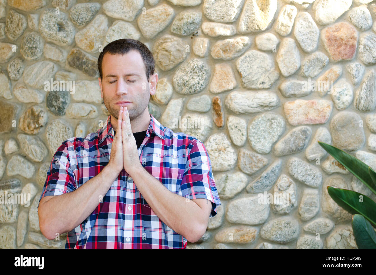 Uomo che prega esterno contro una parete di roccia. Foto Stock