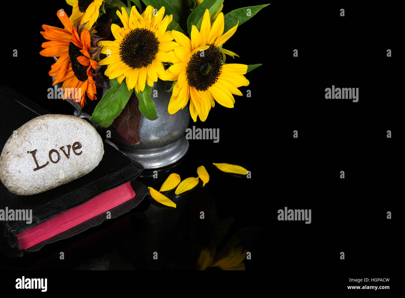 La parola amore scolpito in pietra nera sulla Sacra Bibbia con bouquet di semi di girasole Foto Stock