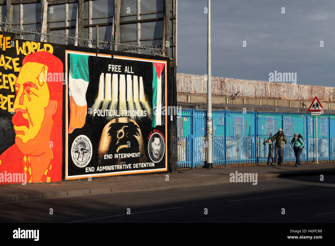 I turisti a piedi giù per la strada scende nella parte occidentale di Belfast passato la pace internazionale nurals parete Foto Stock