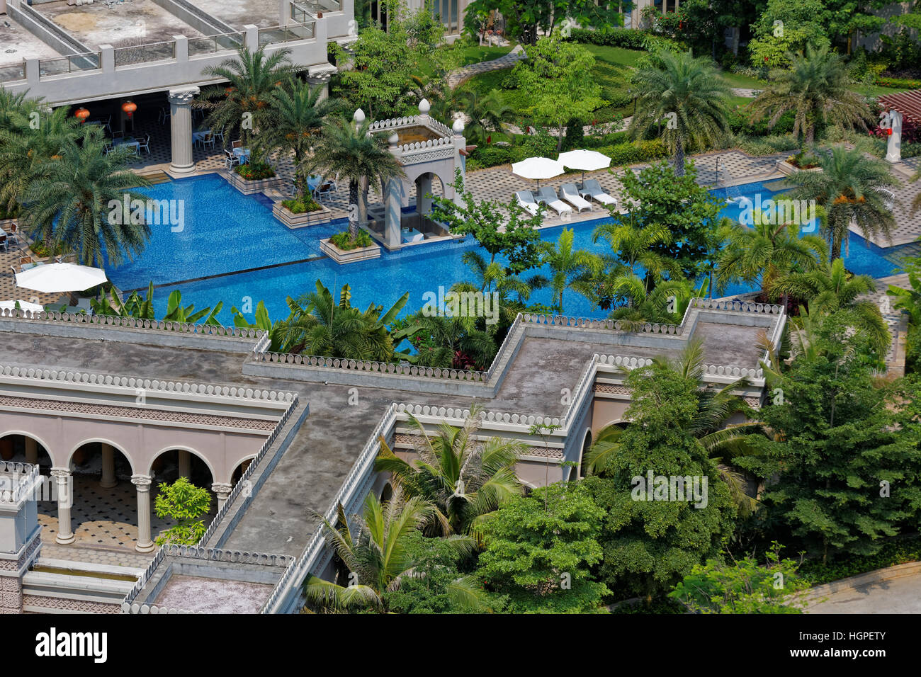 Vista aerea di un moderno hotel aperto piscina con lettini e ombrelloni e palme Foto Stock