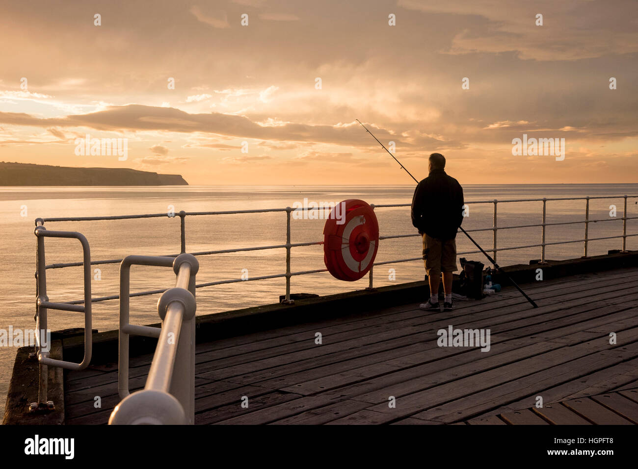 Scenic Whitby & stagliano drammatico, luminoso colorato tramonto cielo, uomo (pescatore) è la pesca in mare dal Molo Ovest - Nord Yorkshire, Inghilterra, Regno Unito. Foto Stock