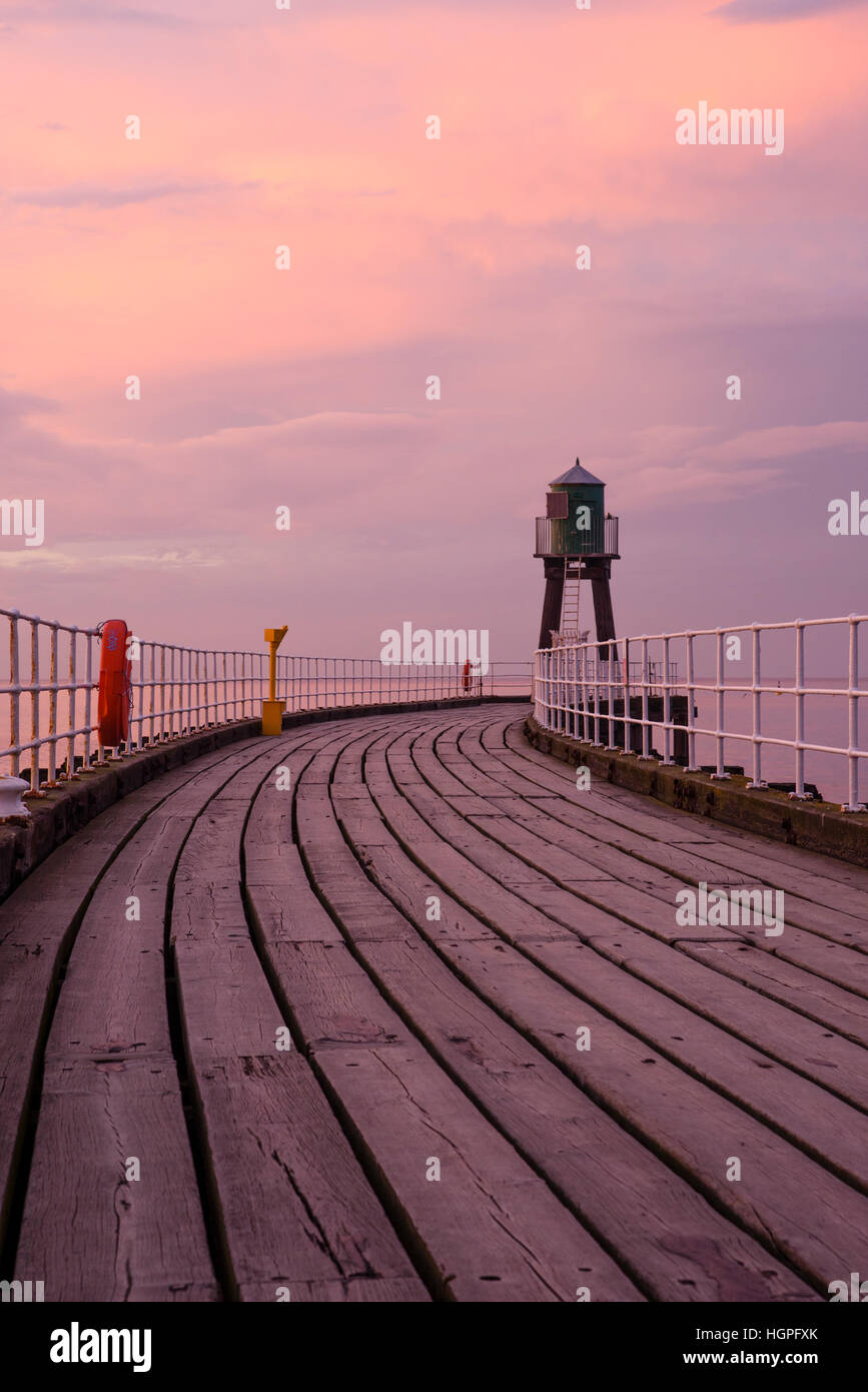 Vista lungo Whitby West Pier estensione, North Yorkshire, Inghilterra - tavole di legno sotto una drammatica rosa, cielo rosso al tramonto. Foto Stock