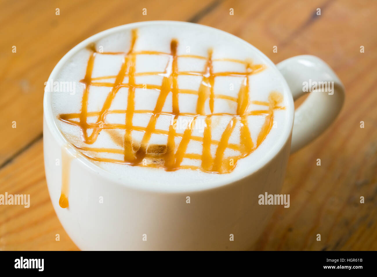 A caldo il caffè macchiato con caramello in tazza bianca sulla tavola di legno dalla luce della finestra Foto Stock