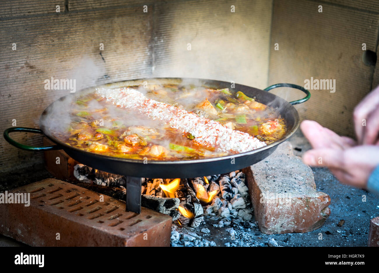 La cottura e la realizzazione di un tradizionale paella spagnola su aprire  il fuoco con il fuoco a legna e a carbone. Realizzato a partire da carne di  pollo e coniglio in