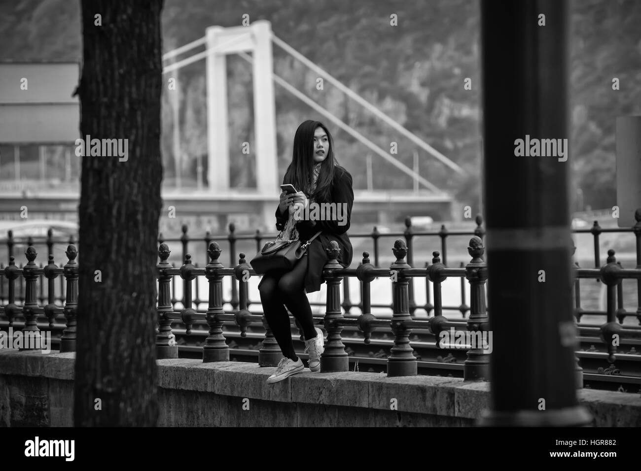 Budapest, Ungheria - Aprile 11,2016: una giovane ragazza cinese seduto sulla recinzione e giocare con il telefono cellulare. Foto Stock