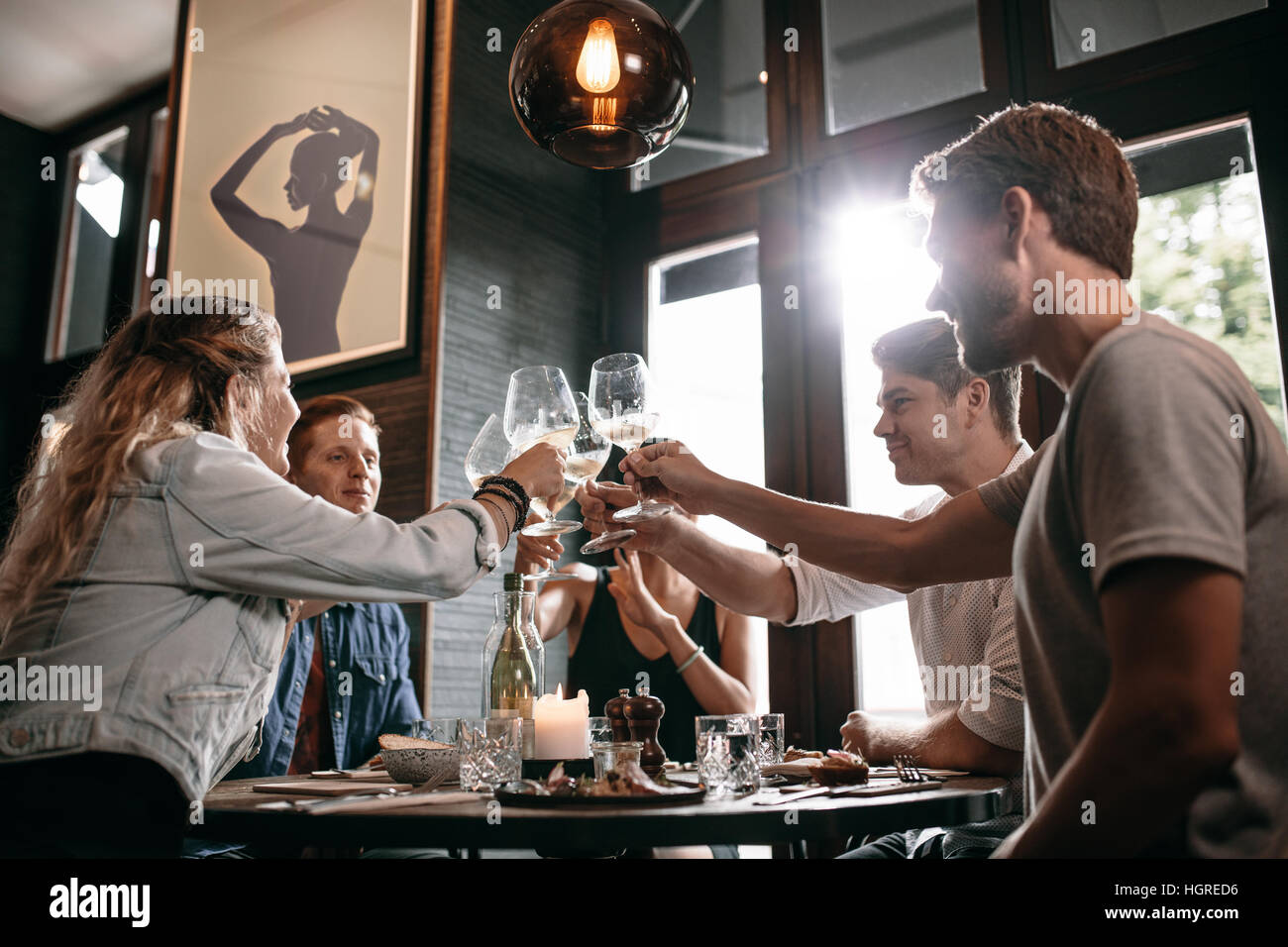 Giovane uomo e donna seduta a tavola e tostatura bevande al ristorante. Il gruppo di amici del vino di tostatura presso il cafe. Foto Stock