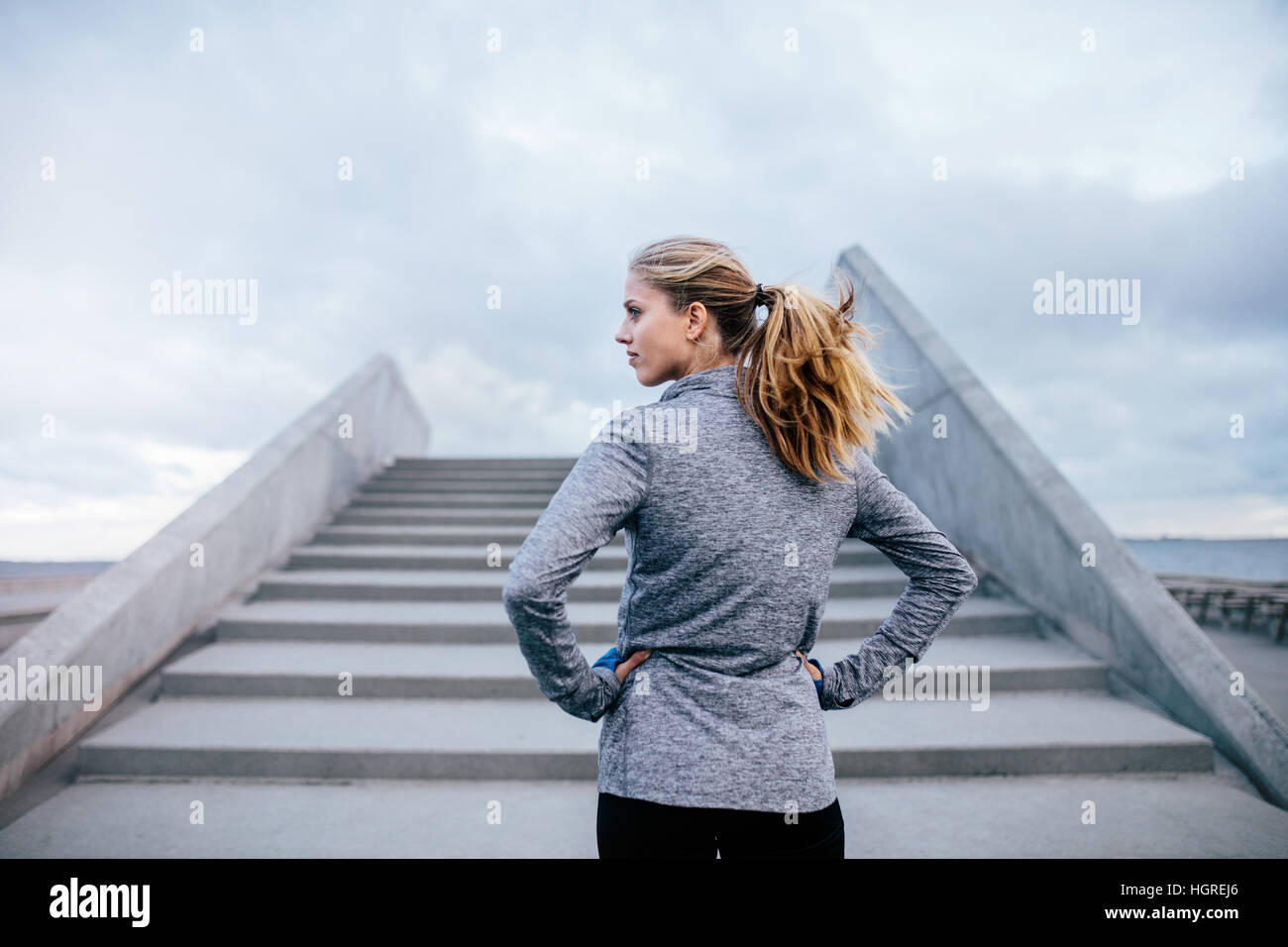 Foto all'aperto di una giovane donna in piedi accanto a una scala e che guarda lontano. fitness femminile prima di una corsa. Foto Stock