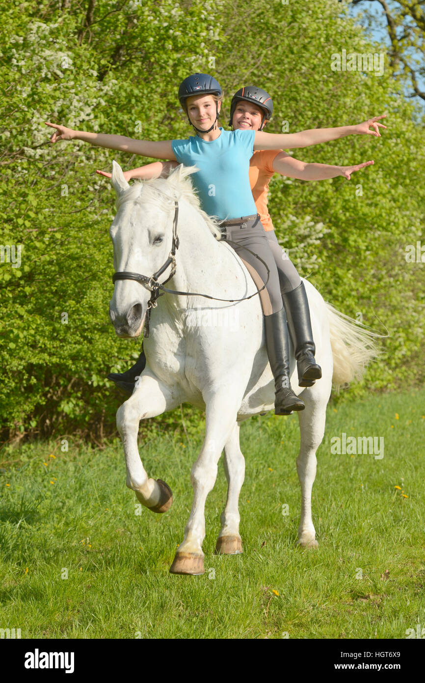 Due giovani horsewomen riding bareback insieme su un cavallo bavarese cantering in primavera Foto Stock