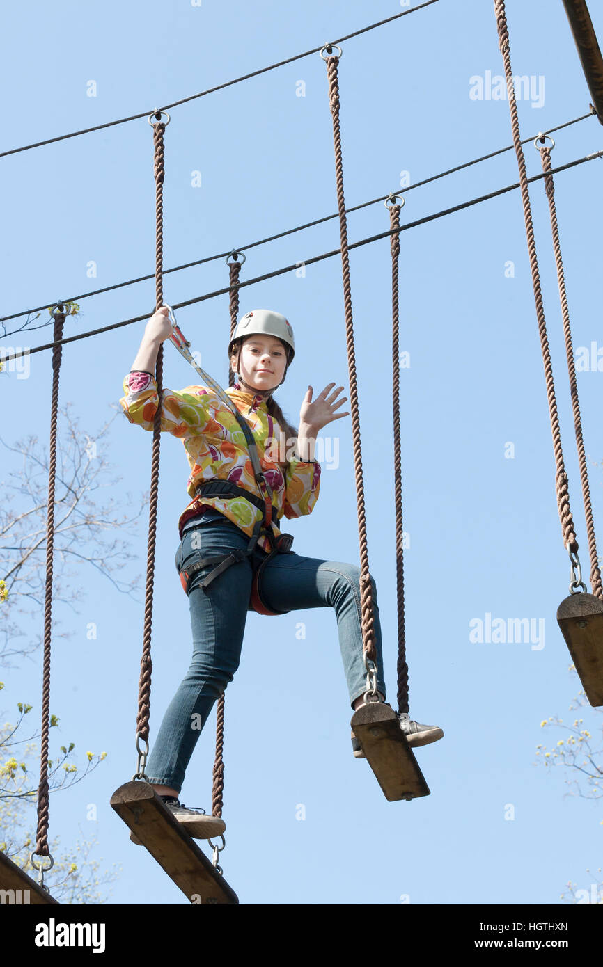 La ragazza si arrampica ostacoli del parco di corda in chiaro giorno di estate Foto Stock