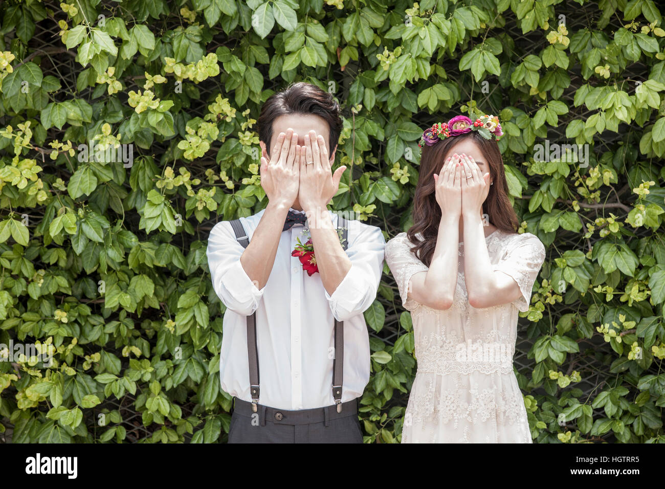 Coppia giovane che coprono i loro volti con le loro mani per matrimonio foto all'aperto Foto Stock