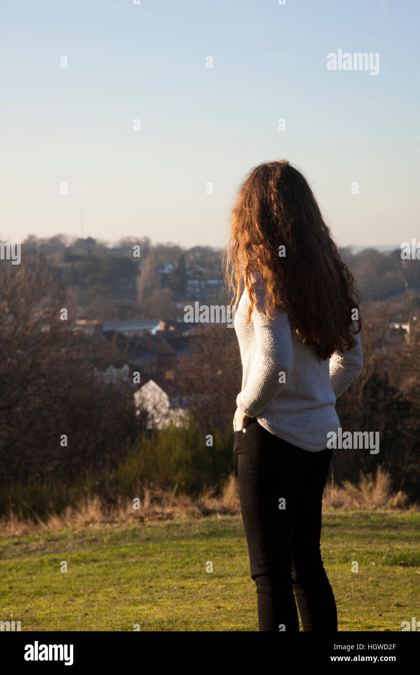Giovane donna con capelli lunghi in piedi torna alla fotocamera, guardando in lontananza. Tre quarti di lunghezza. Foto Stock