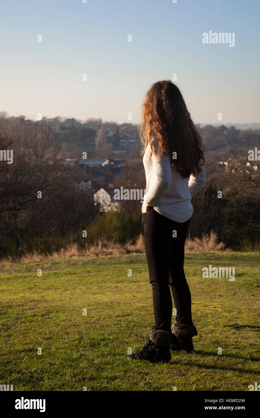 Giovane donna con capelli lunghi in piedi torna alla fotocamera, guardando in lontananza. Lunghezza intera. Foto Stock