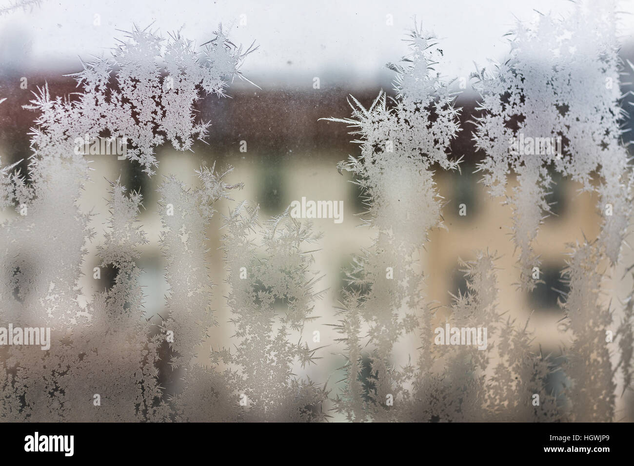 I cristalli di ghiaccio sulla finestra con vista delle case della città durante il periodo invernale Foto Stock