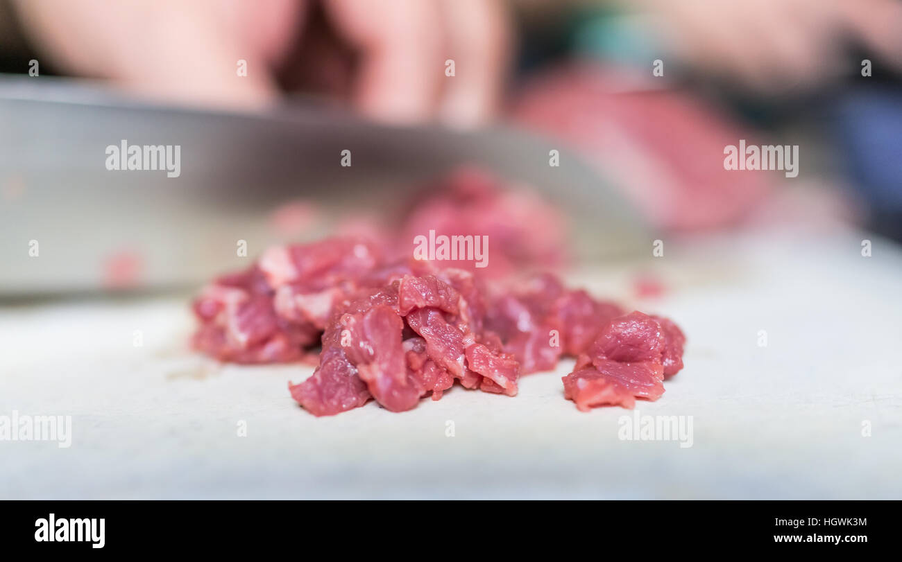 Le mani con grande coltello di taglio di carne di manzo strisce in pezzi Foto Stock