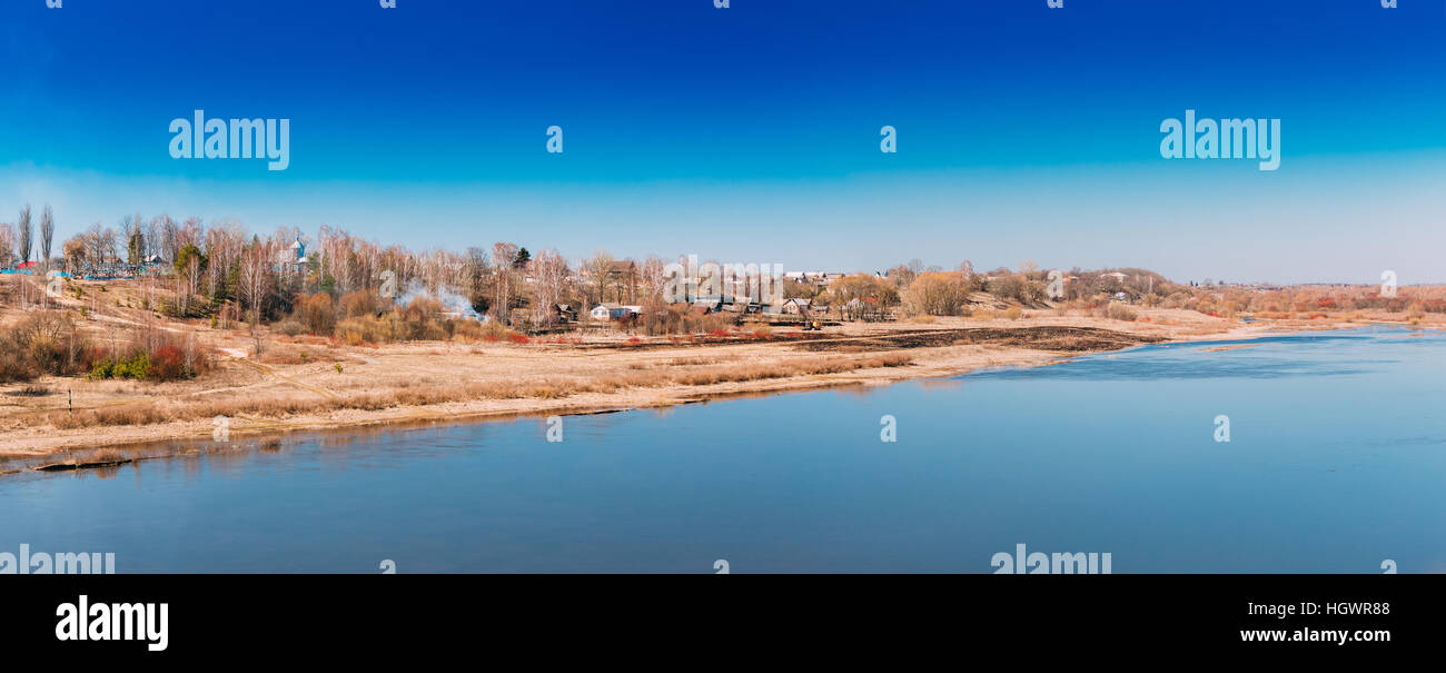 Vista panoramica del villaggio sulla collina ricoperta vicino ingiallito Riverbank In Primavera / Autunno giornata soleggiata sotto il blu cielo chiaro. Copia dello spazio. Panorama Foto Stock