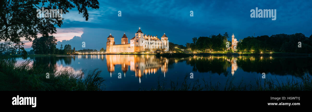 Mir, Bielorussia. Scenic Vista panoramica del complesso del Castello di Mir In illuminazione serale dal lato del lago. Famoso punto di riferimento, antico monumento in Blue di DRAM Foto Stock
