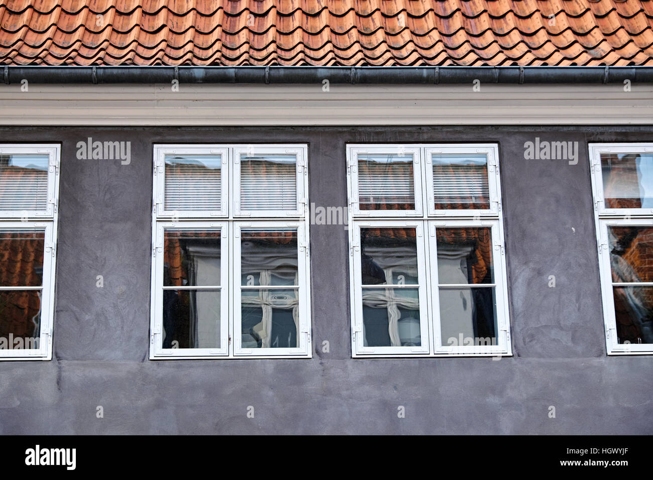 Grigio facciata intonacata con dipinto di bianco di doppie finestre a battente, di legno sopra è un tetto rosso con piastrelle in argilla e una grondaia di zinco Foto Stock