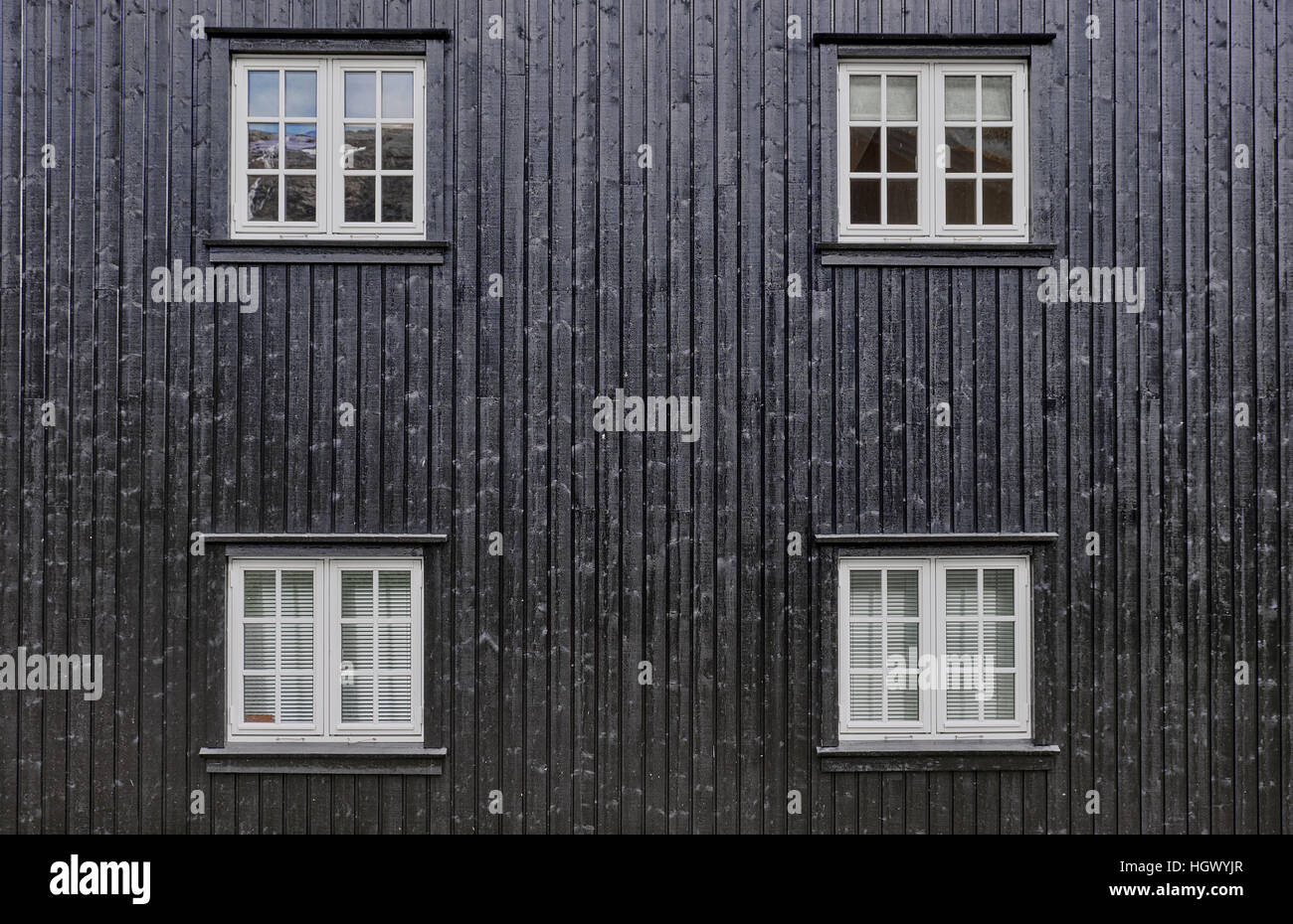 Quattro quadrati di bianco le finestre a battente con montanti, disposte simmetricamente in un dipinto di nero facciata con pannelli montati come linguetta e scanalatura Foto Stock