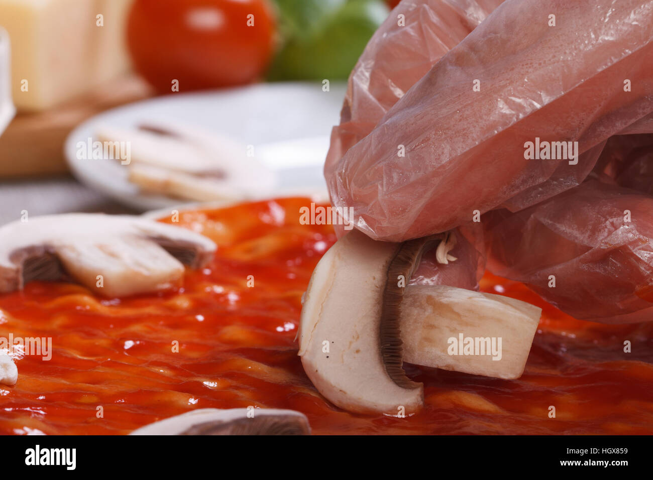 Mano nel guanto chef mette su una base per pizza funghi champignon. macro Foto Stock