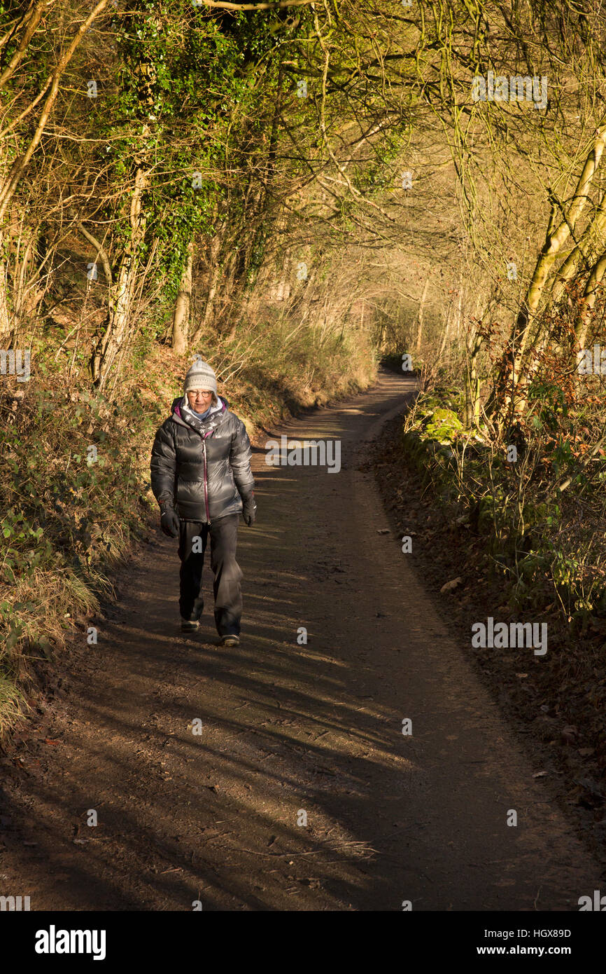 Regno Unito, Inghilterra, Derbyshire, Cressbrook, femmina senior walker sulla corsia a Ravensdale Cottages in inverno Foto Stock