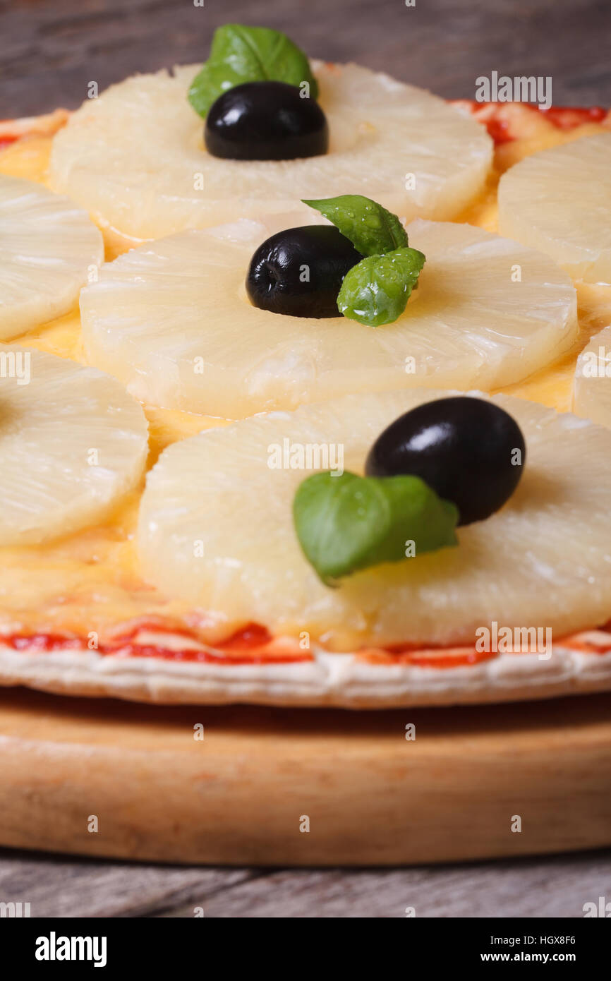 Pizza con ananas, olive nere e il verde del basilico sul vecchio tavolo. primo piano verticale. Foto Stock