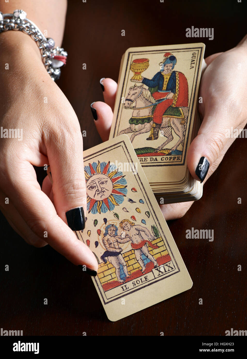 Vista ravvicinata mani femminili con nero Nail art e del bracciale che mostra vecchia carta dei tarocchi e il mazzo di carte su tavolo scuro Foto Stock