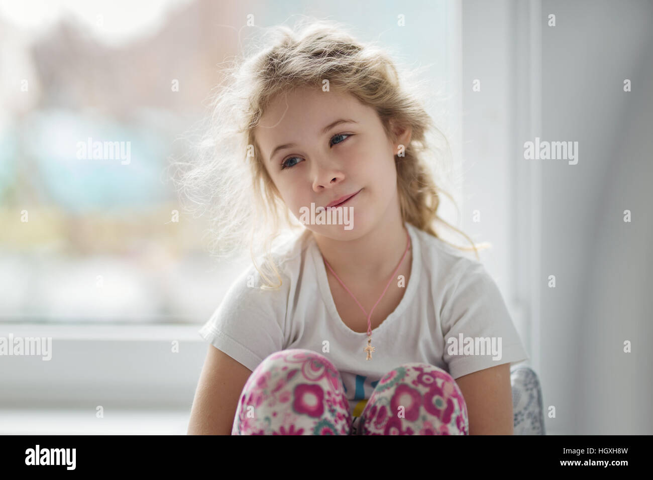 Ritratto di carino bambino biondo ragazza seduta vicino alla finestra Foto Stock
