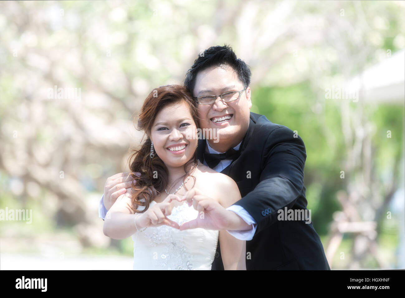 Ritratto di Allegro sposi abbracciando e mostra forma di cuore. Asian sposi in giardino Foto Stock