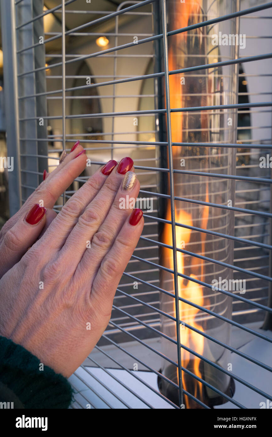 La donna si scalda le mani su una strada moderna fire. Foto Stock