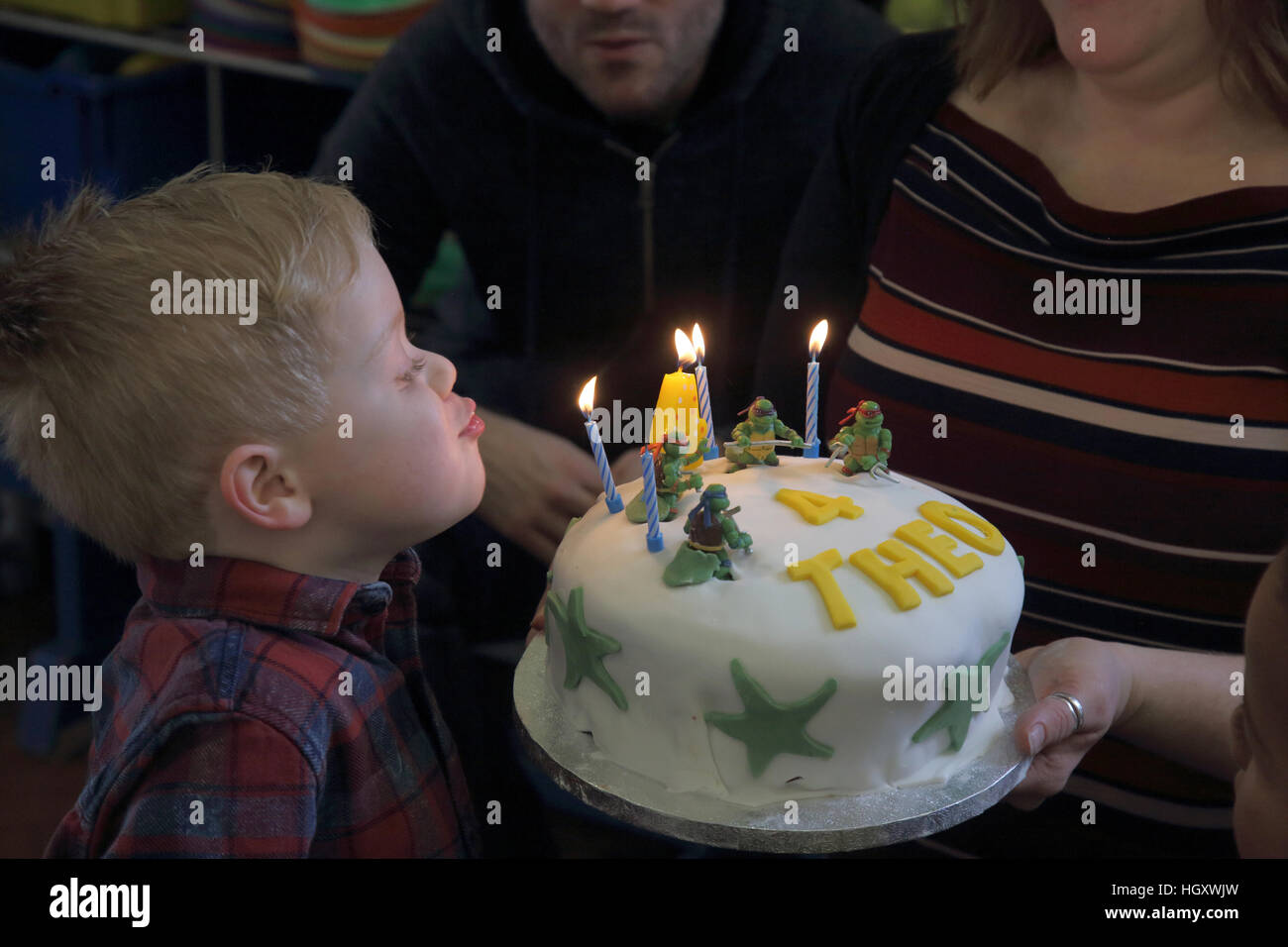Ragazzo giovane soffiando fuori candele sulla quarta torta di compleanno Foto Stock