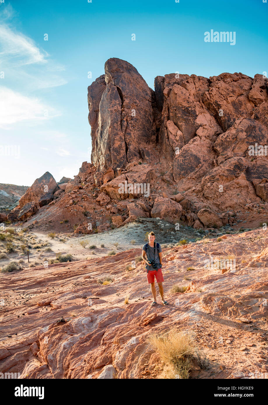 Giovane uomo escursionismo, rosso formazioni rocciose nella luce della sera, rocce di arenaria, la Valle del Fuoco, Deserto Mojave, Nevada, STATI UNITI D'AMERICA Foto Stock
