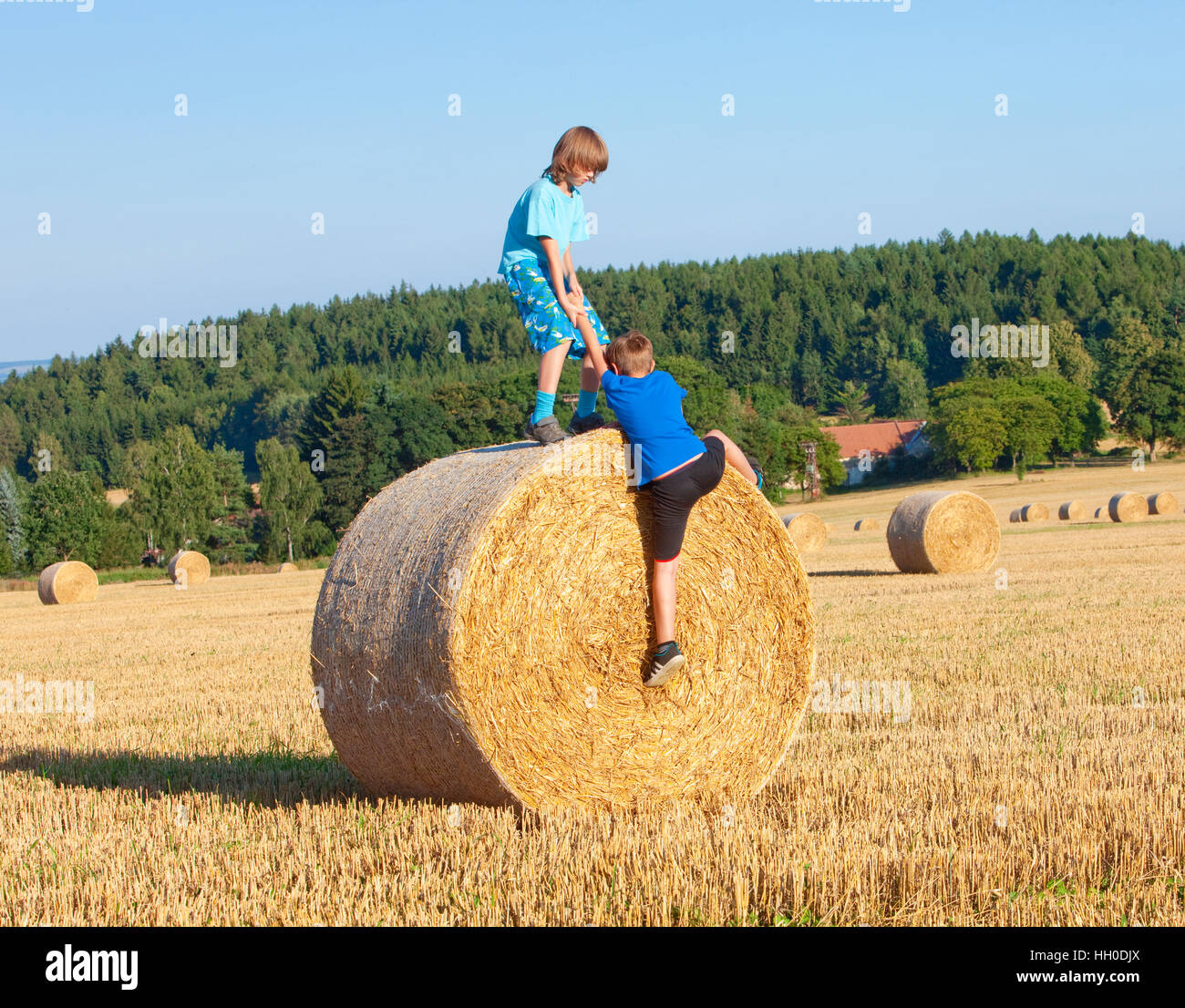 Due ragazzi che si aiutano reciprocamente per salire su una balla di fieno Foto Stock