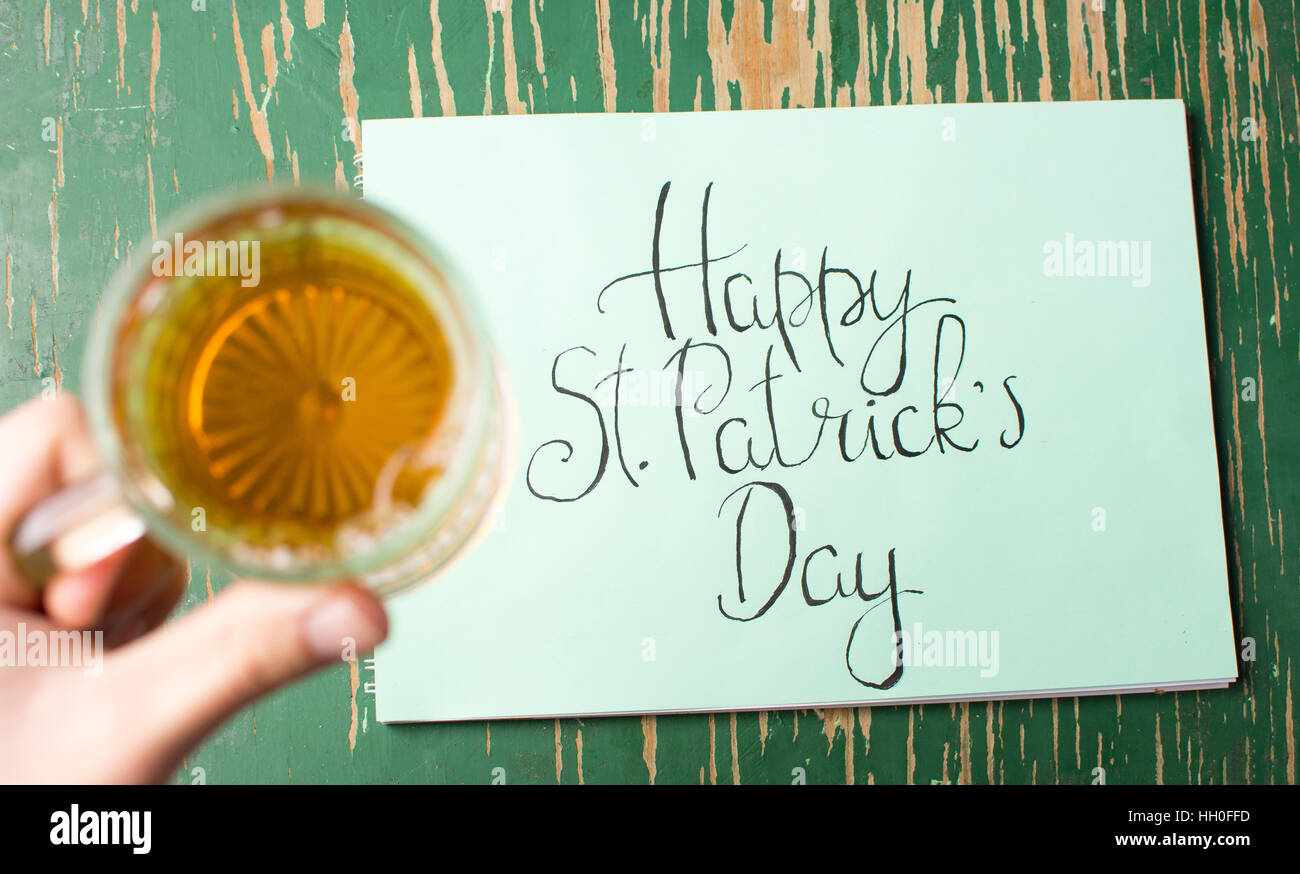 Happy St Patrick giorno scheda di calligrafia e birra in mano Foto Stock