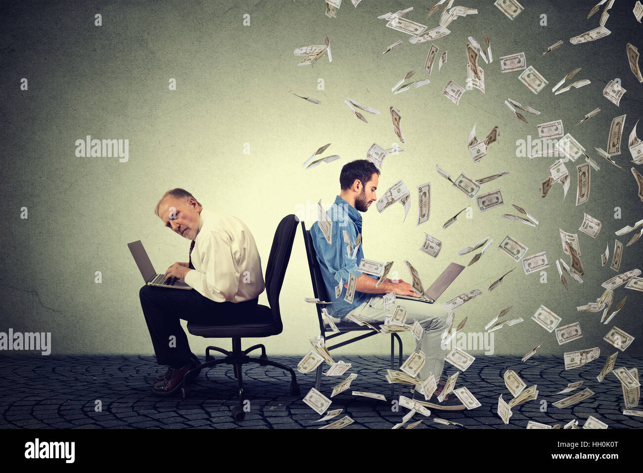 Compensazione del dipendente il concetto di economia. Senior uomo al lavoro su laptop seduto accanto al giovane imprenditore guy sotto la pioggia di denaro. Foto Stock