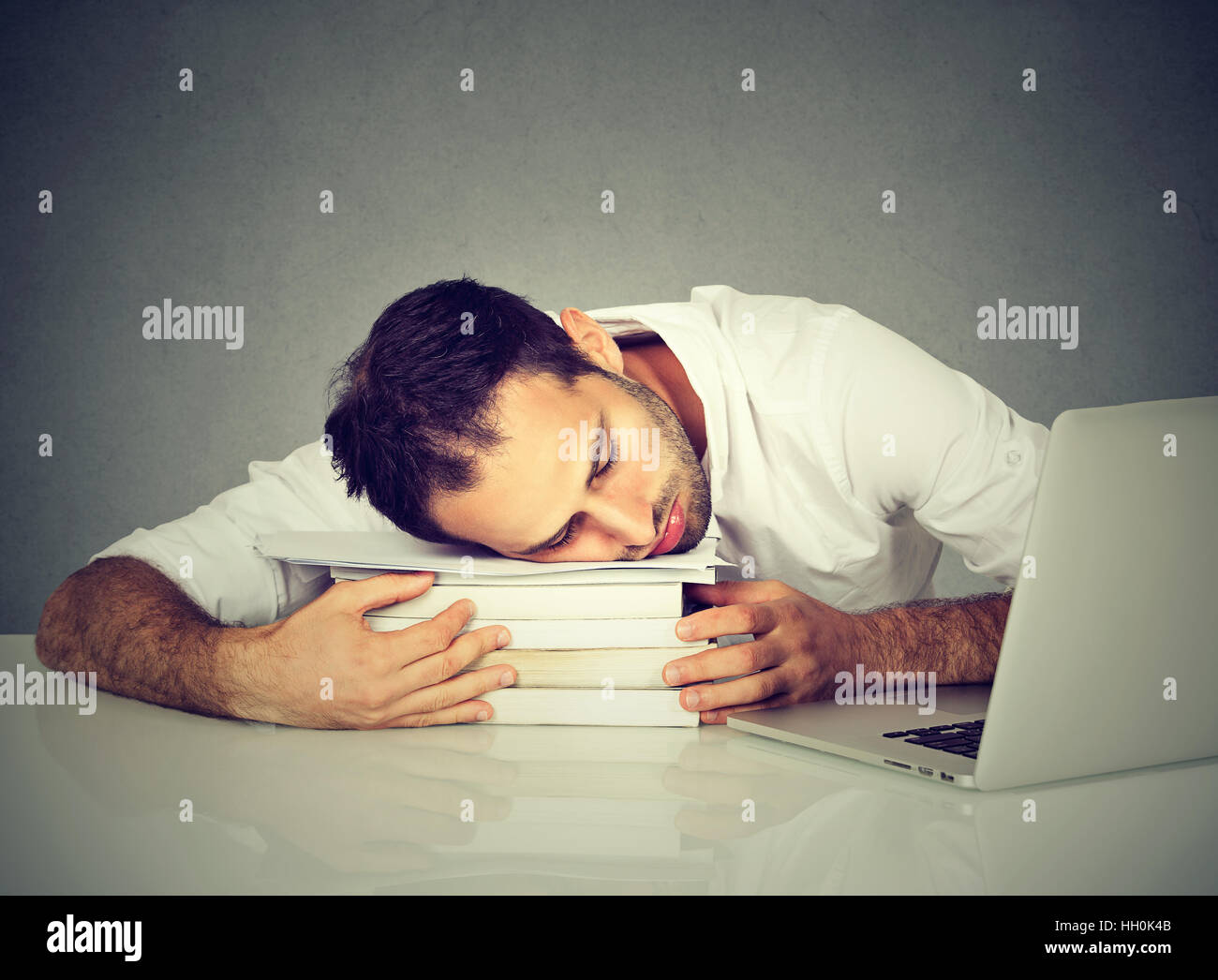 Troppo lavoro uomo stanco di dormire su libri al desk nella parte anteriore del computer. Pianificazione di occupato in un college, il lavoro, la privazione del sonno Foto Stock