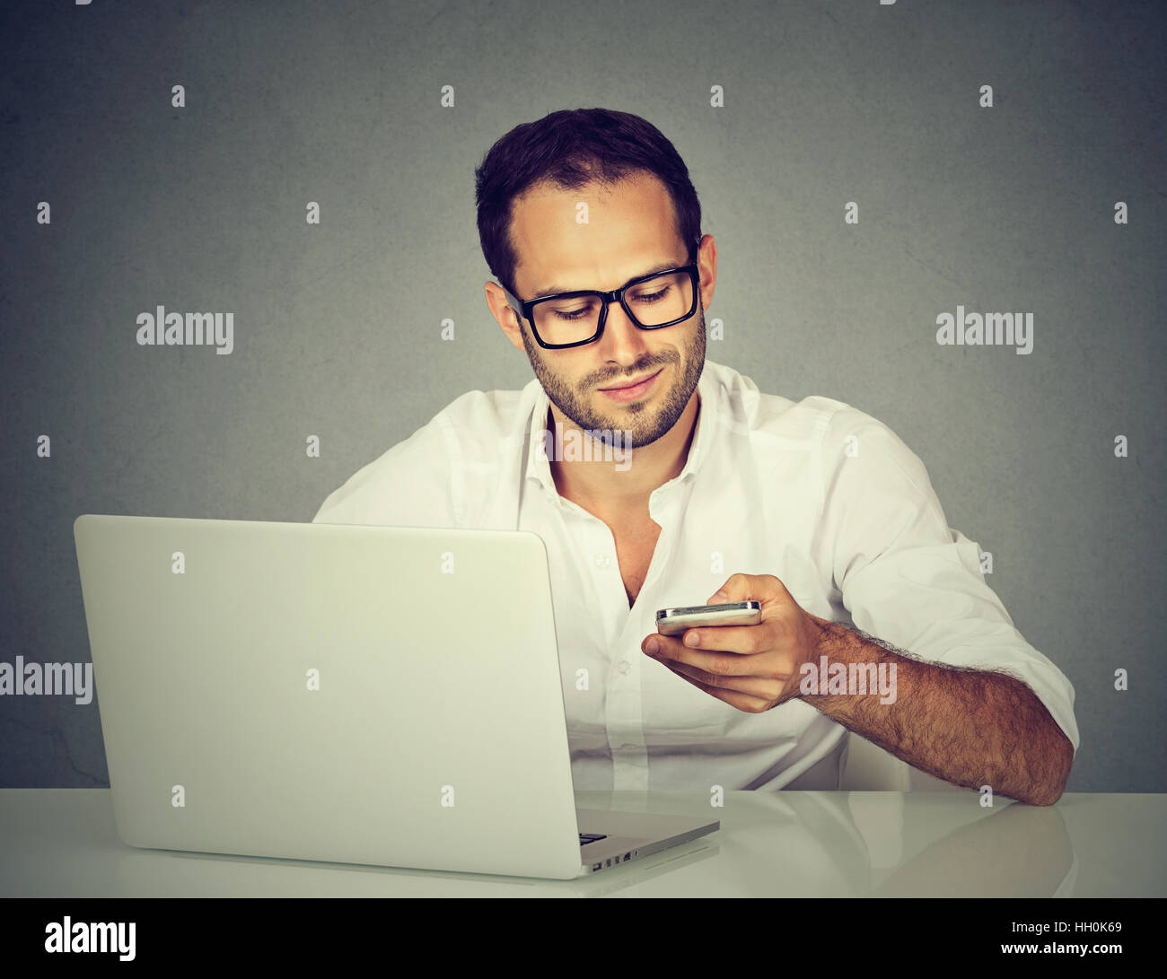 Giovane uomo con notebook sms sul cellulare seduta a tavola Foto Stock