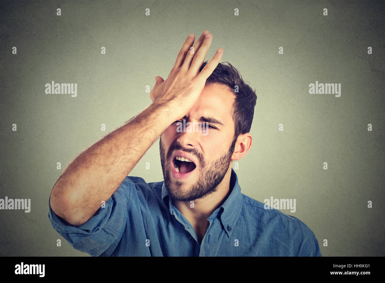 Si rammarica del fatto di sbagliato facendo. Silly, man mano che sbatte sulla testa avente una duh momento isolato su sfondo grigio. Negativo emozione umana Foto Stock