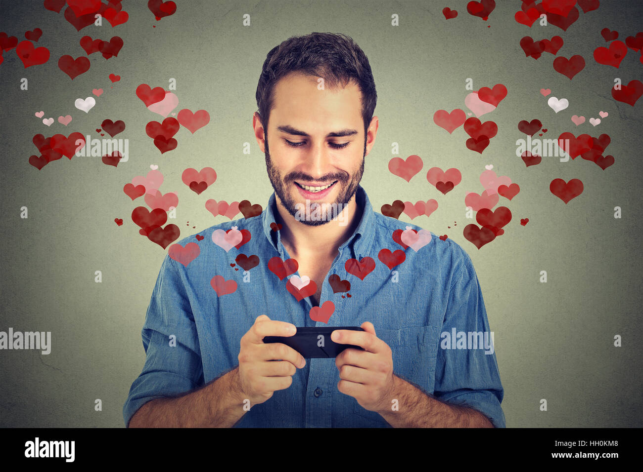 Uomo felice amore invio messaggio sms sul cellulare cuori rossi volare lontano dalla schermata isolati uno sfondo grigio. Emozione umana Foto Stock