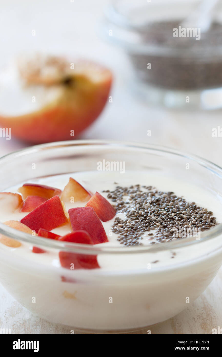 Yogurt con pesche, chia semi in ciotola di legno bianco sullo sfondo. Dieta di luce prima colazione Foto Stock